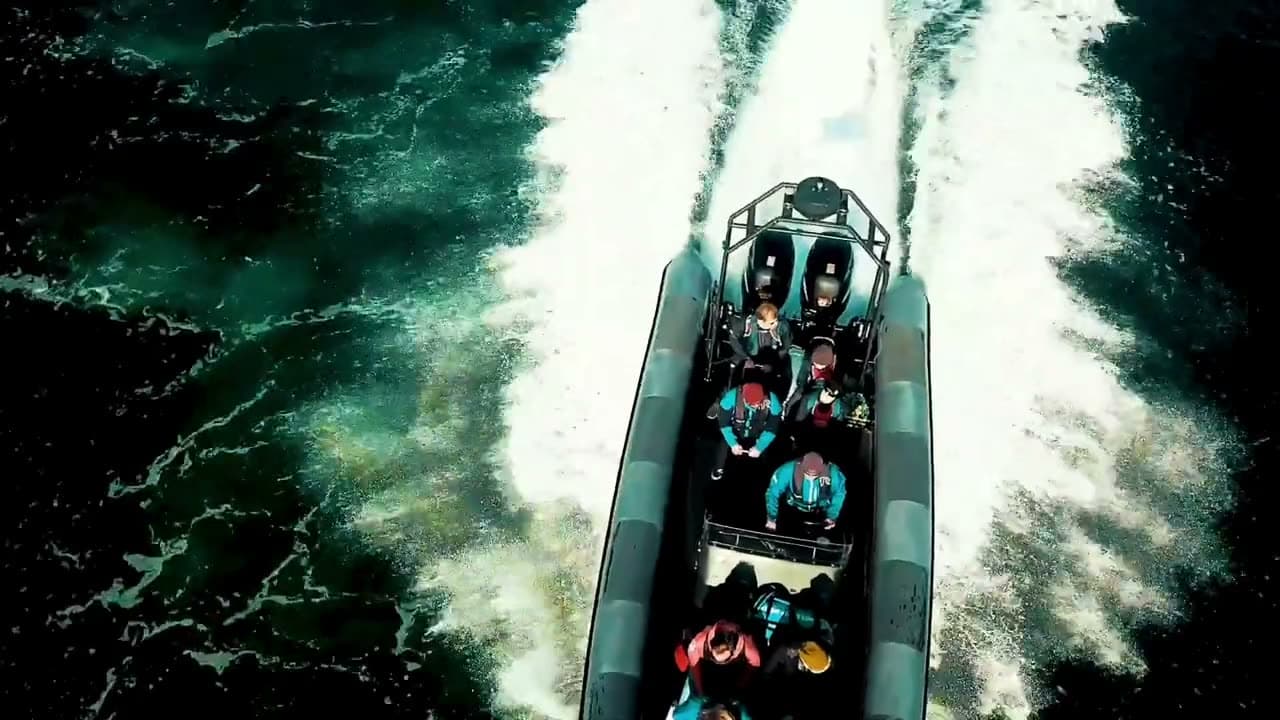 En RIB full av gjester i gule flytedresser i full fart forbi skjærene, fotografert fra båten ved siden av