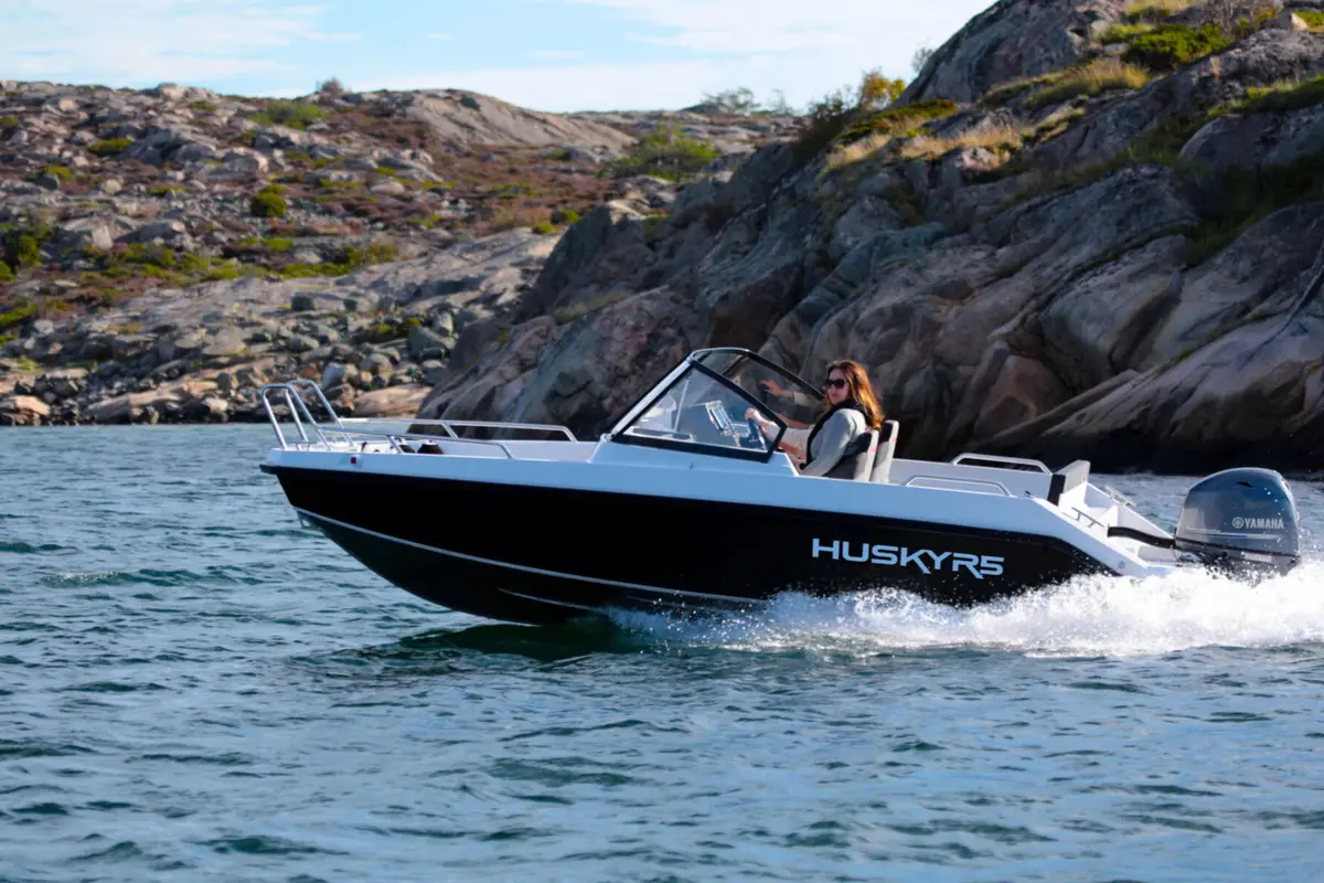 En liten motorbåt ved svaberg i solskinn